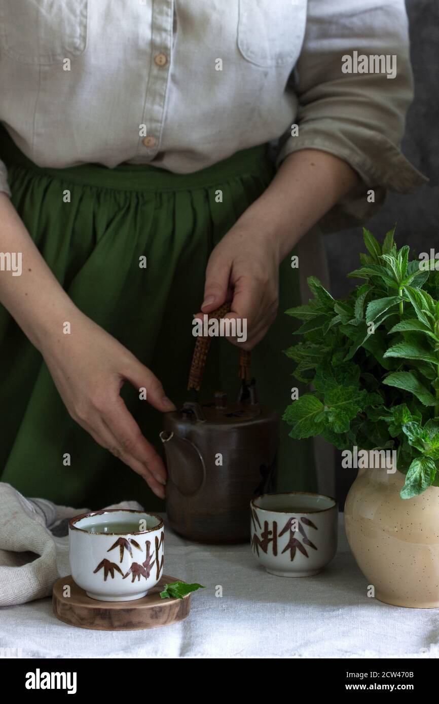 Tè alla menta in un set da tè cinese d'epoca, una donna in un abito di lino e un grembiule, e un bouquet di menta in una caraffa. Foto Stock