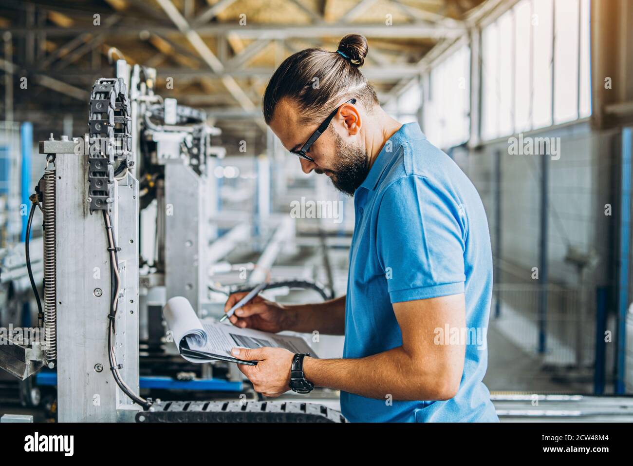 Un operatore in occhiali in prossimità di apparecchiature industriali e  verifica i dati di produzione. Uomo che tiene la cartella nelle mani Foto  stock - Alamy