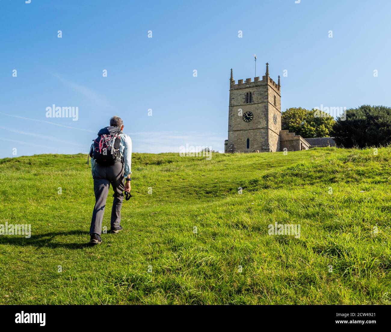 Walker che sale alla chiesa di San Giovanni Battista sul collina a Old Sodbury sulla Cotswold Way in Gloucestershire REGNO UNITO Foto Stock