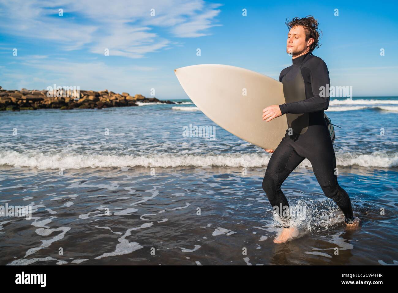Ritratto di giovane surfista che lascia l'acqua con tavola da surf sotto il braccio. Concetto di sport e sport acquatici. Foto Stock
