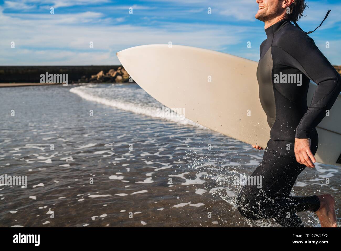 Ritratto di giovane surfista che lascia l'acqua con tavola da surf sotto il braccio. Concetto di sport e sport acquatici. Foto Stock