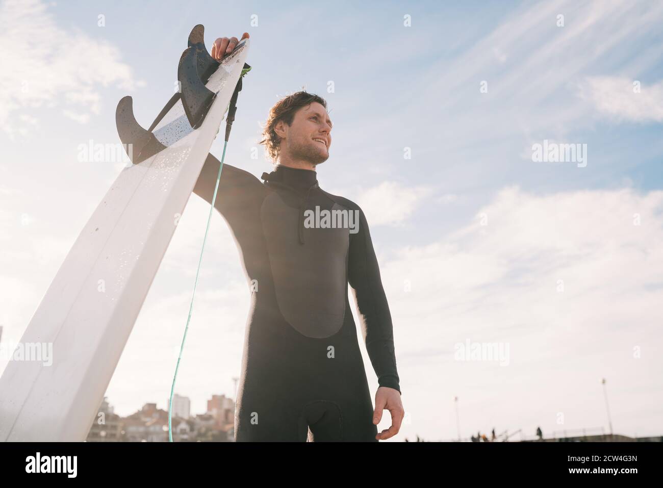 Primo piano di un giovane surfista in spiaggia con la sua tavola da surf e il costume da surf nero. Concetto di sport e sport acquatici. Foto Stock