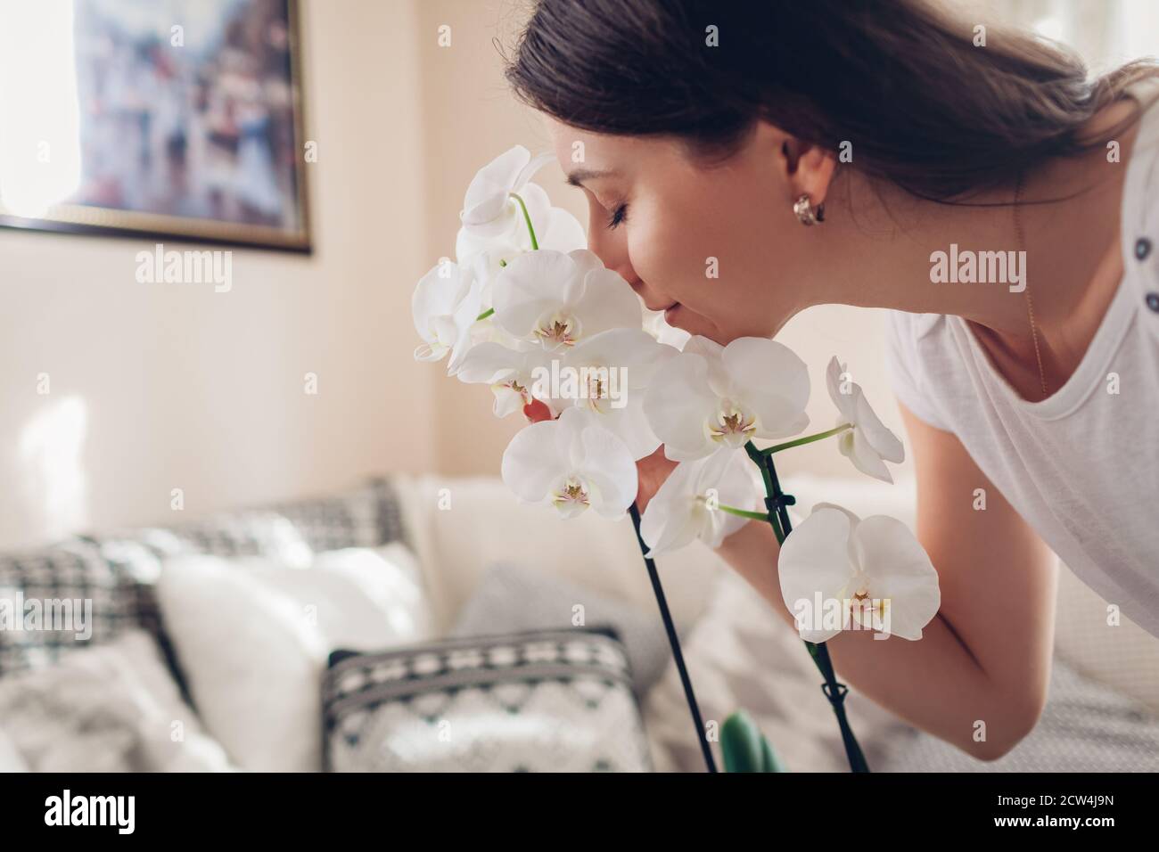 Donna che puzzava orchidea bianca in fiore nel soggiorno. Casalinga che prende cura di piante e fiori domestici. Interno Foto Stock