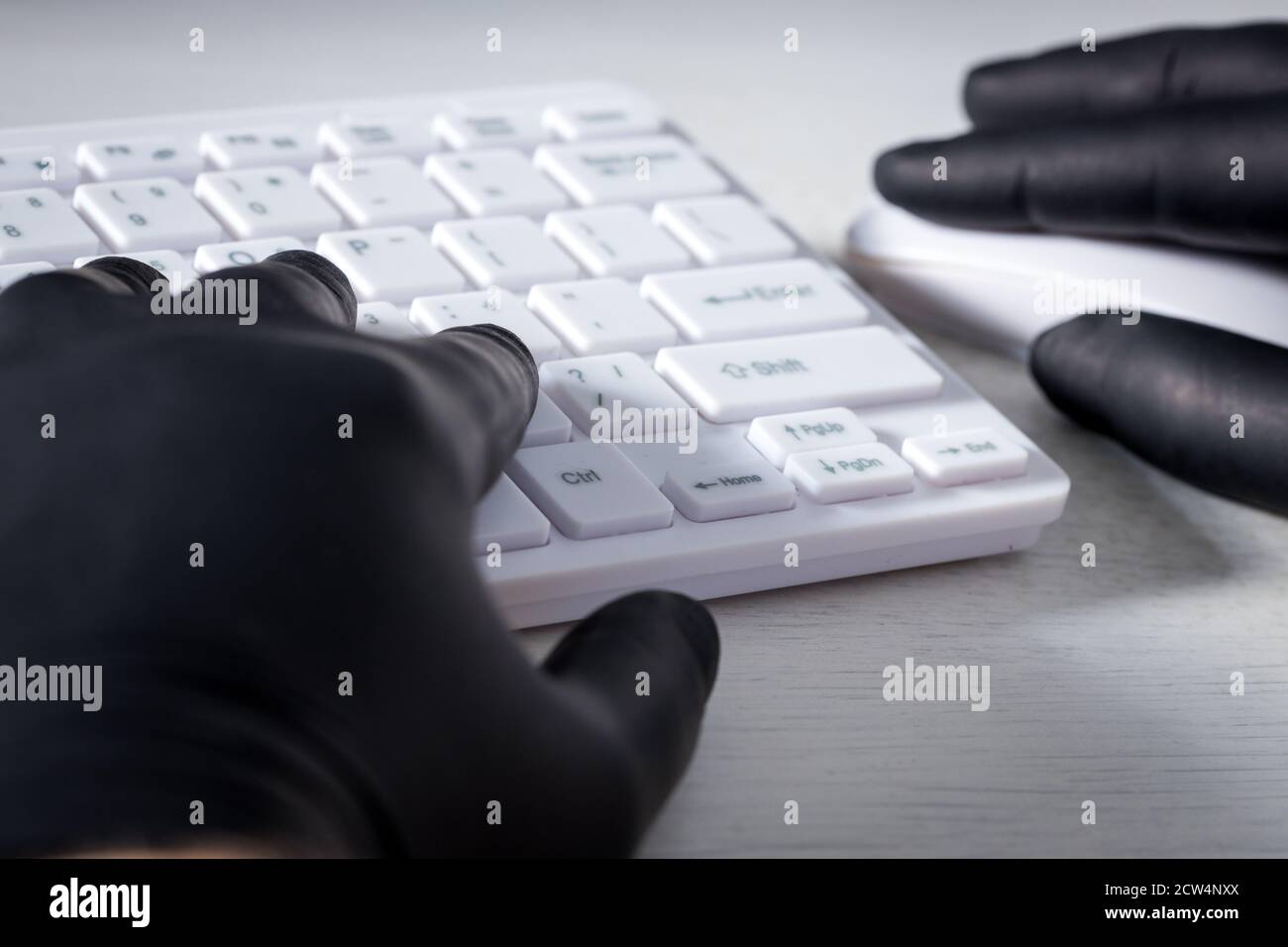 Tastiera e mani bianche del computer in guanti di gomma nera. Concetto di criminalità e molestie sul web Foto Stock