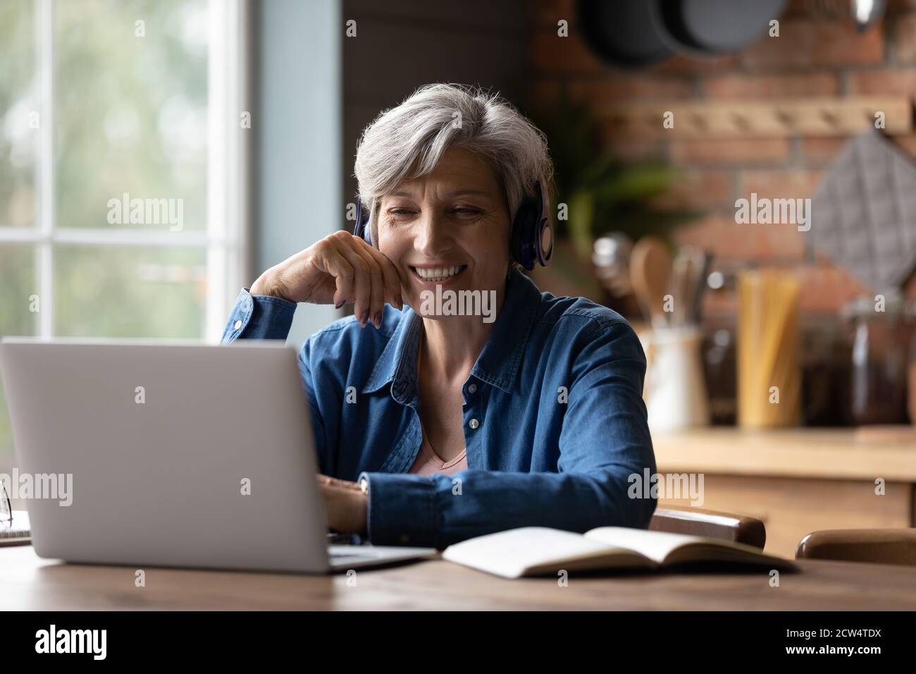 Donna anziana intelligente in cuffia: Guarda il webinar sul notebook Foto Stock