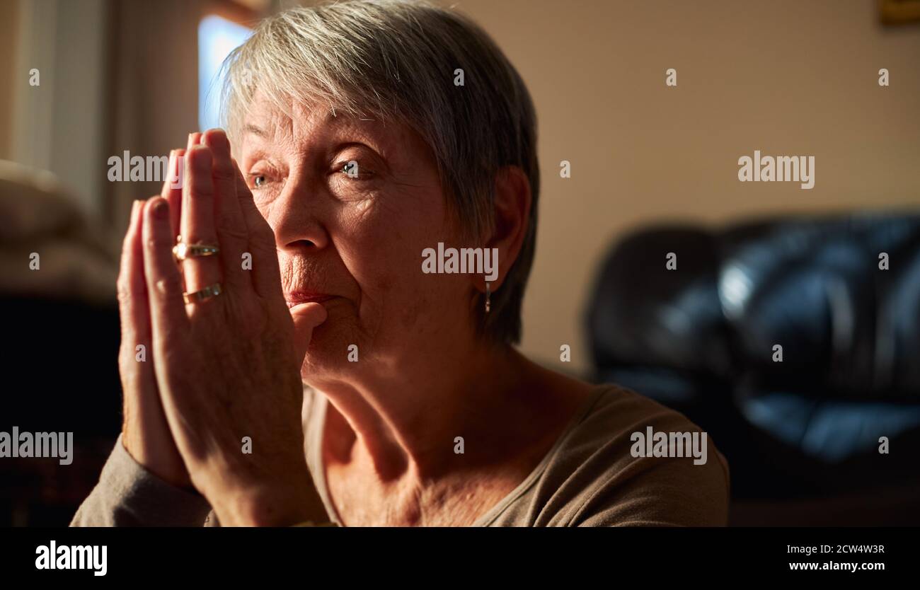 Primo piano di Senior Woman a casa in preghiera o meditating Con le mani insieme Foto Stock