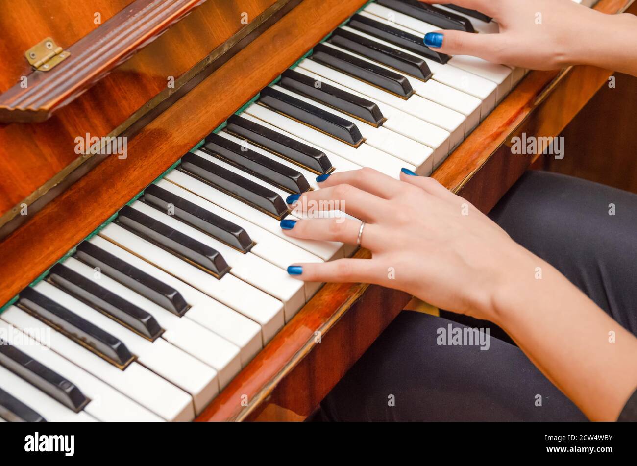 Mani di una pianista femminile con unghia blu polacca sui chiodi sulle chiavi di un pianoforte. Ragazza che suona il pianoforte. Foto Stock