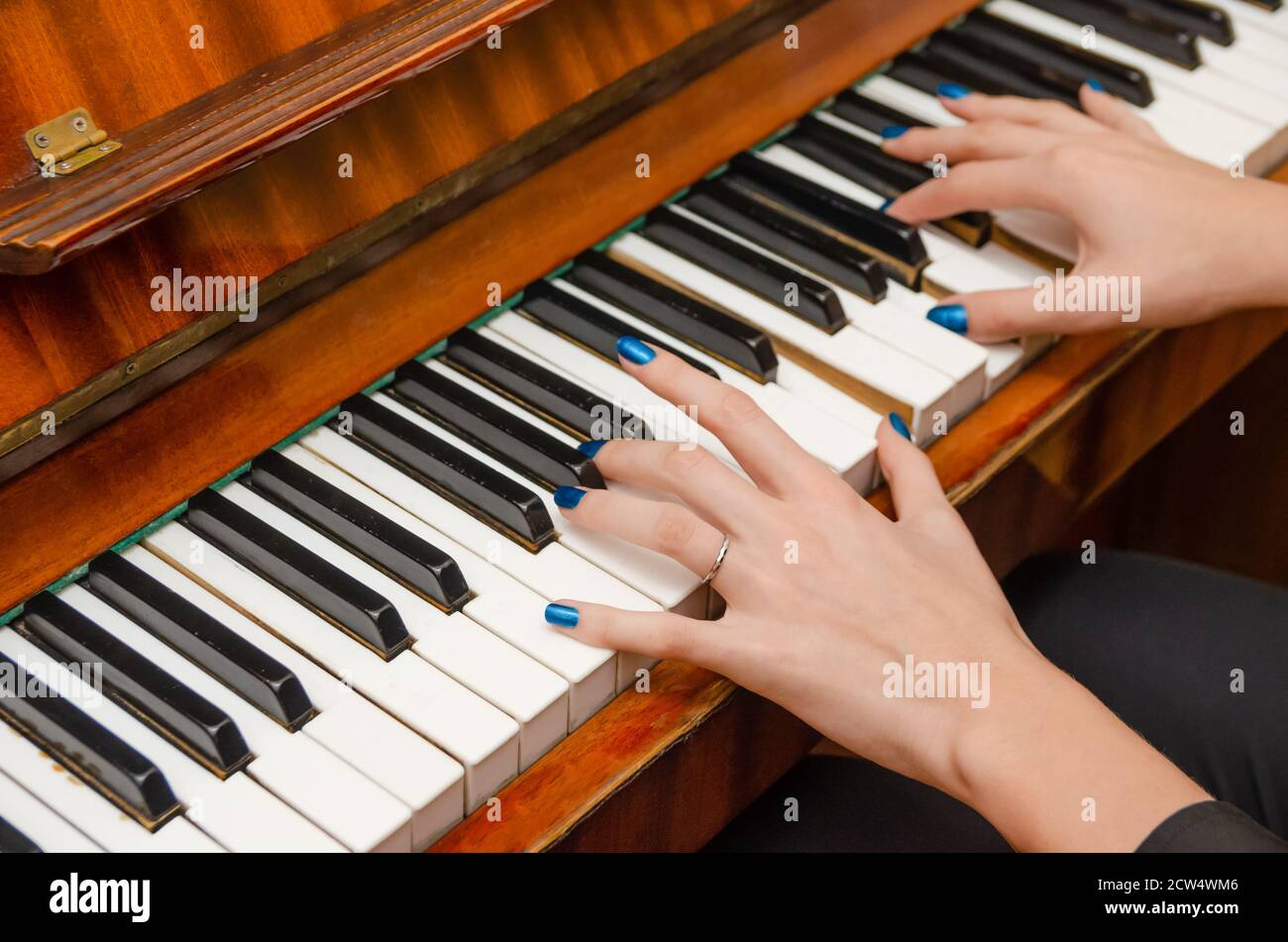 Mani di una pianista femminile con unghia blu polacca sui chiodi sulle chiavi di un pianoforte. Ragazza che suona il pianoforte. Foto Stock