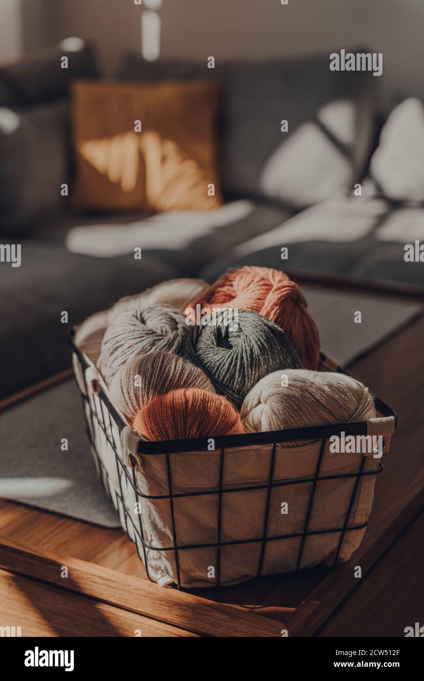 Palle di filato colorato di terra all'interno di un cesto su un tavolo all'interno di un appartamento, luce solare dalla finestra su di esso, fuoco selettivo. Foto Stock