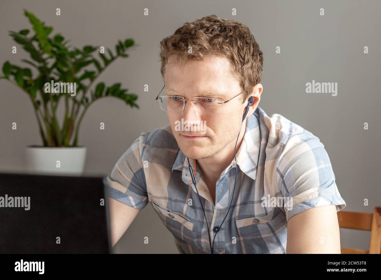 Programmatore in cuffia che lavora da casa, da remoto, da casa. Un uomo con occhiali guarda il monitor. Concetto di lavoro remoto - immagine Foto Stock