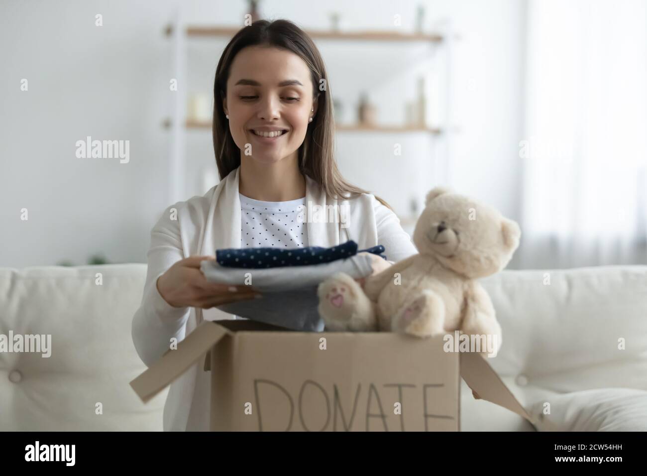 Gentile giovane donna raccogliere scatola di donazione con vestiti Foto Stock