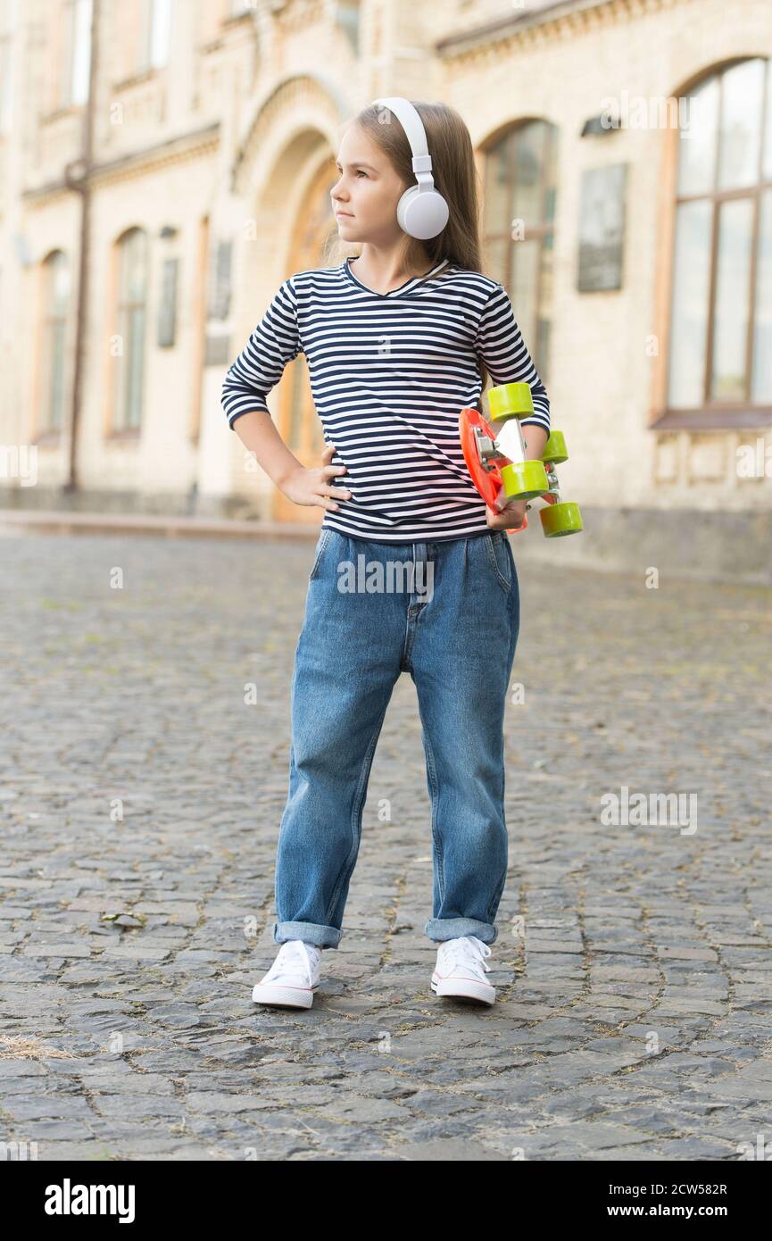 Fuggi con un penny skateboard. Il piccolo skater ascolta la musica con le cuffie. Piccolo bambino tenere penny board. Skateboard di strada. Velocità ed equilibrio. Trasporto. Avventura viaggio. Vacanze estive. Foto Stock