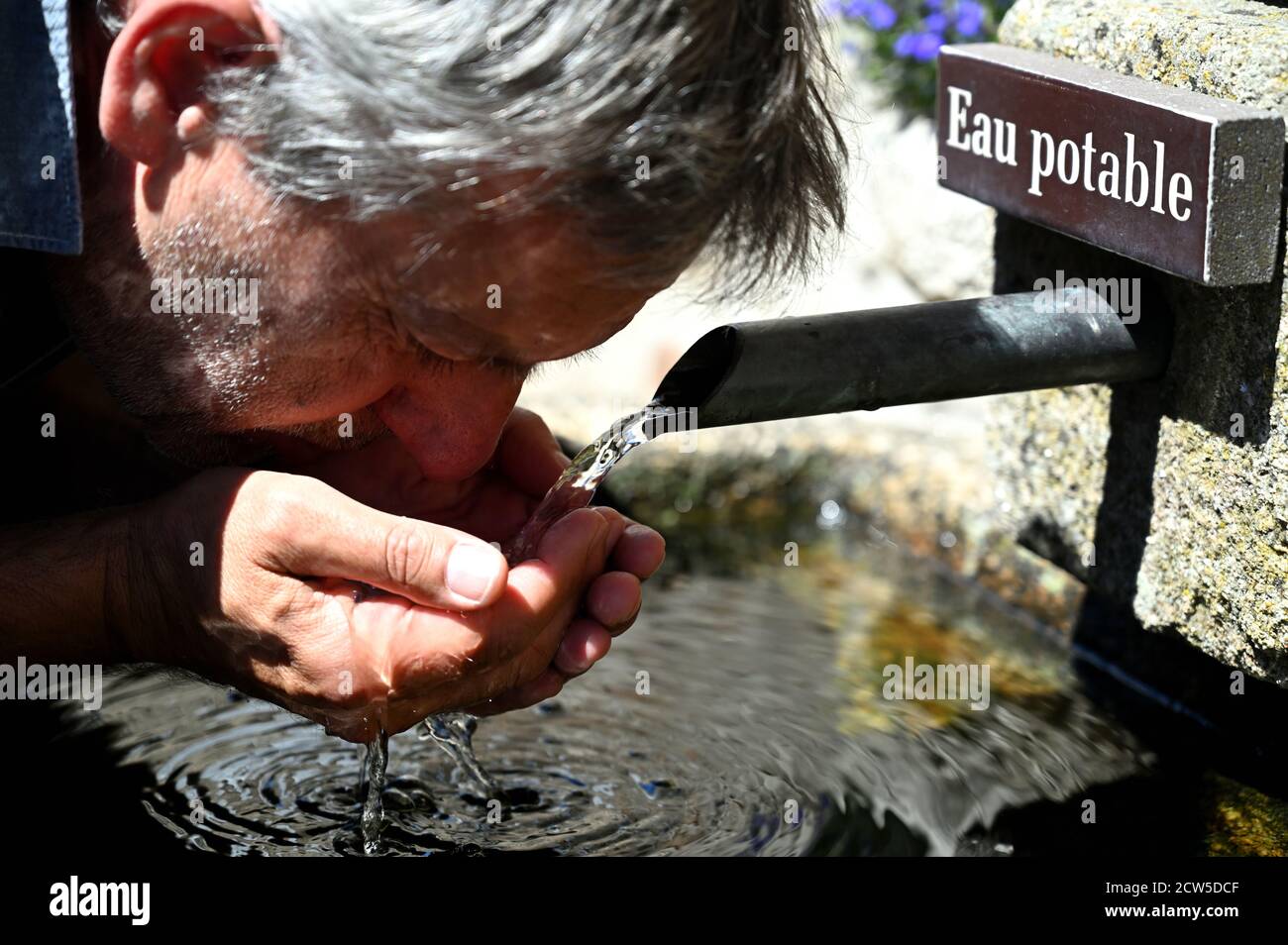 Uomo che beve acqua da una fontana pubblica. Traduzione : 'Eau potable' significa acqua potabile Foto Stock
