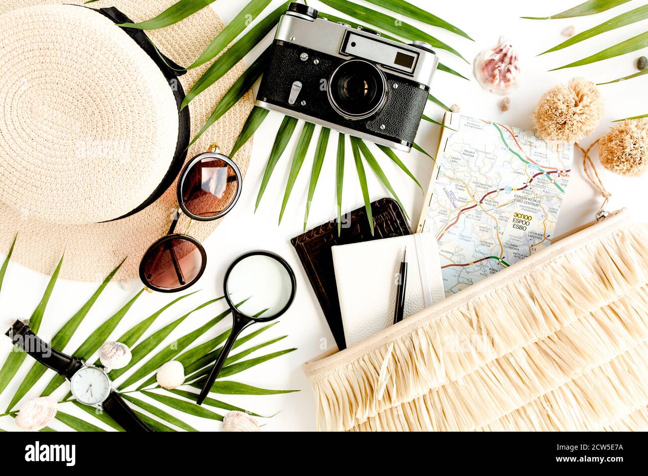 Accessori per viaggiatori su sfondo bianco con fotocamera retrò, cappello di paglia, borsa, occhiali da sole, mappa e foglia di palma tropicale. Foto Stock