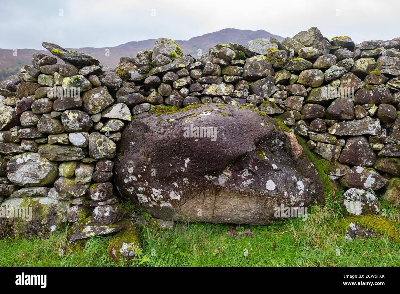 Muro di pietra a secco costruito intorno e su un grande masso irregolare - Lake District, Inghilterra, Regno Unito Foto Stock