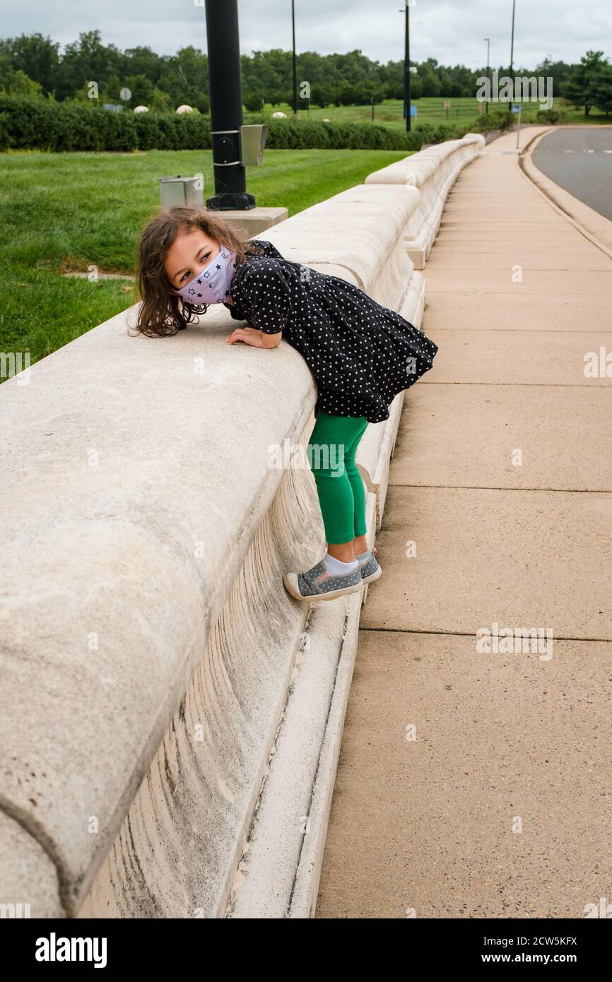 Bambina con maschera che gioca all'esterno durante la pandemia del coronavirus Foto Stock