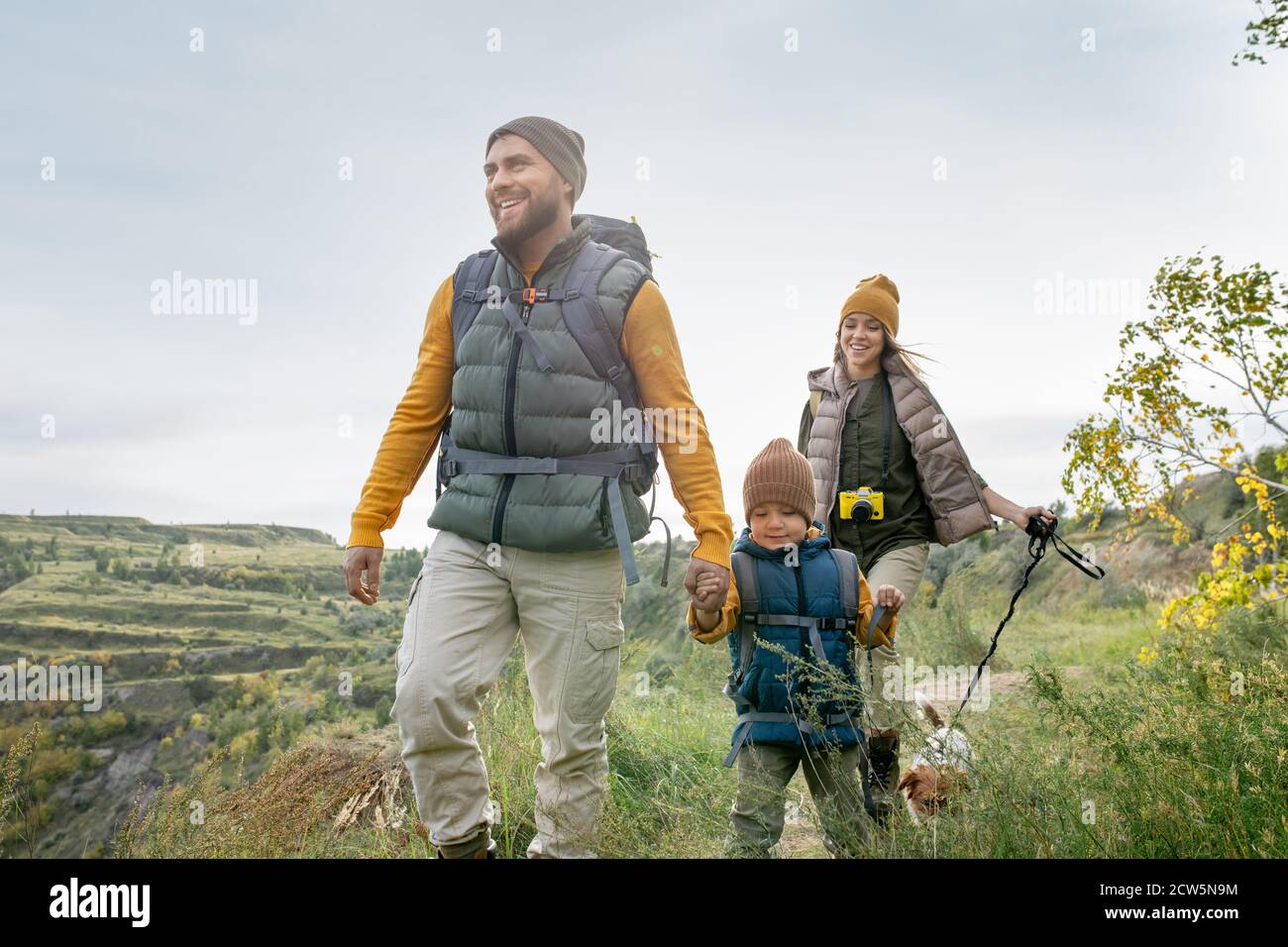 Tre backpackers felici in casualwear caldo e il loro animale domestico carino viaggio piacevole Foto Stock