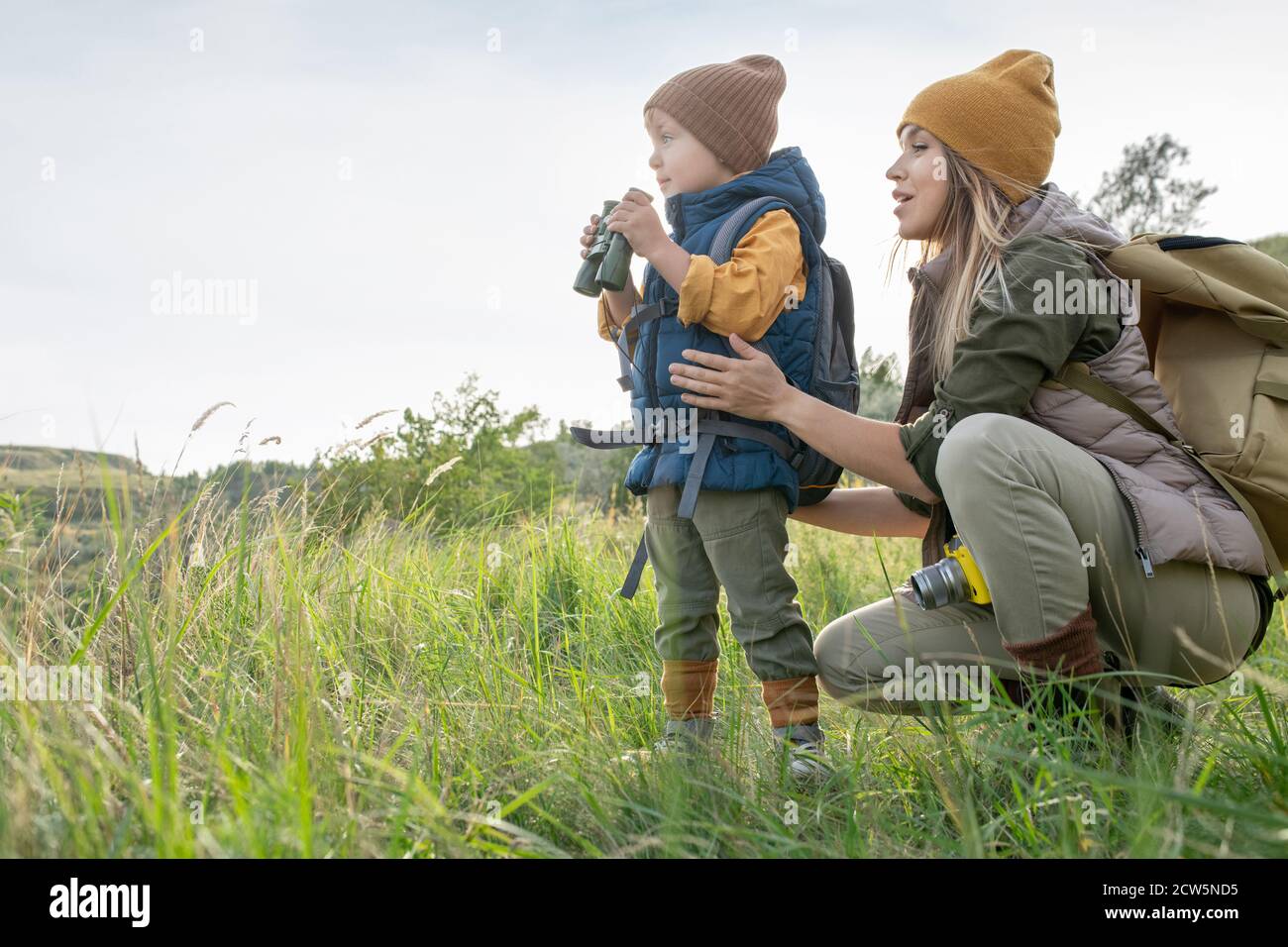 Giovane donna con zaino squatting da suo figlio piccolo con binocoli in viaggio Foto Stock