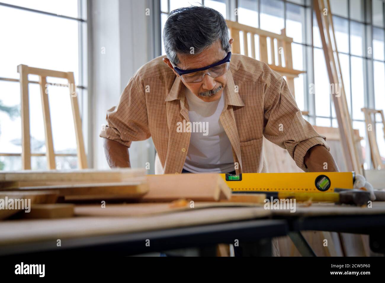 L'uomo anziano asiatico usa l'attrezzo di livello per misurare la superficie di legno in officina di Falegnameria. Foto Stock