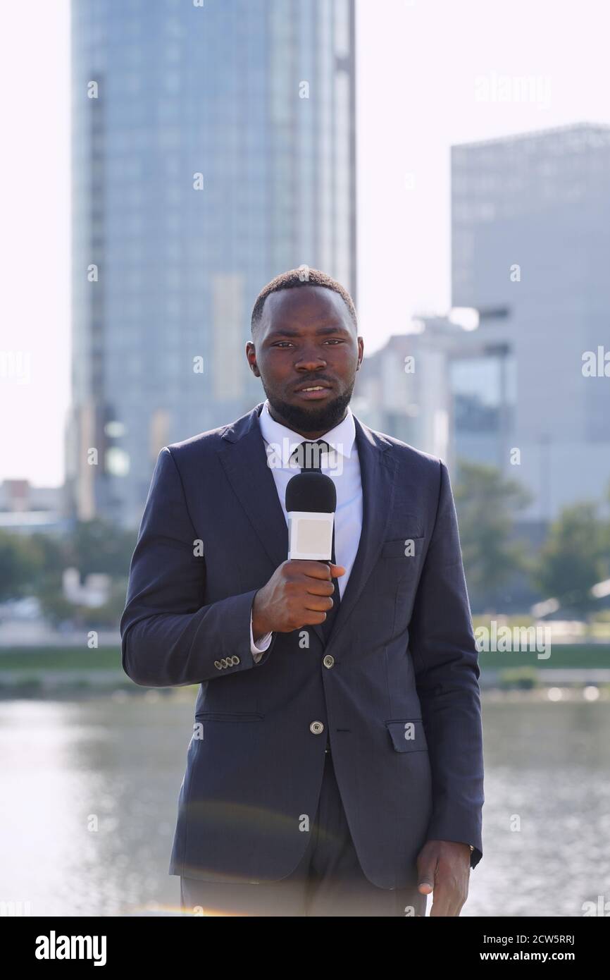 Felice giovane ed elegante reporter di etnia africana che parla al microfono Foto Stock