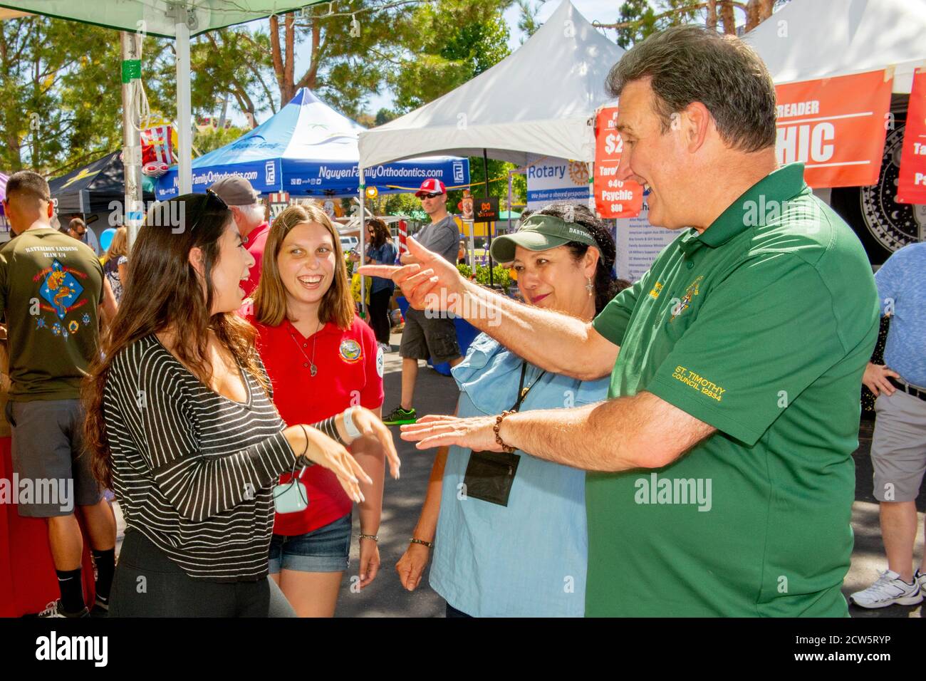 Un diacono cattolico socializza con i giovani parrocchiani durante una mostra di fuorilegge di una fiera di strada a Laguna Niguel, CA. Foto Stock