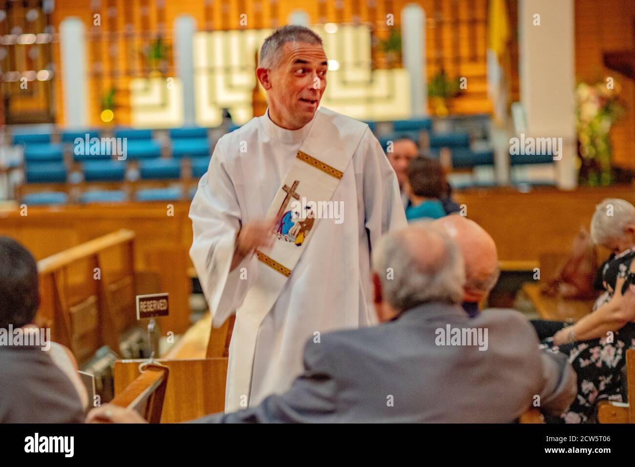 Un diacono robato socializza con i parrocchiani in pews prima di un matrimonio in una chiesa cattolica della California meridionale. Foto Stock