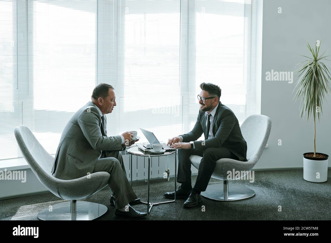 Due uomini d'affari maturi e sicuri in abbigliamento da formalwear che discutono dei momenti di lavoro Foto Stock
