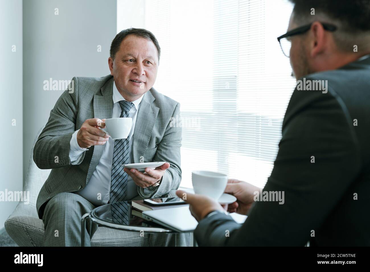 Uomo d'affari sicuro e maturo in formalwear avendo caffè e guardando partner Foto Stock