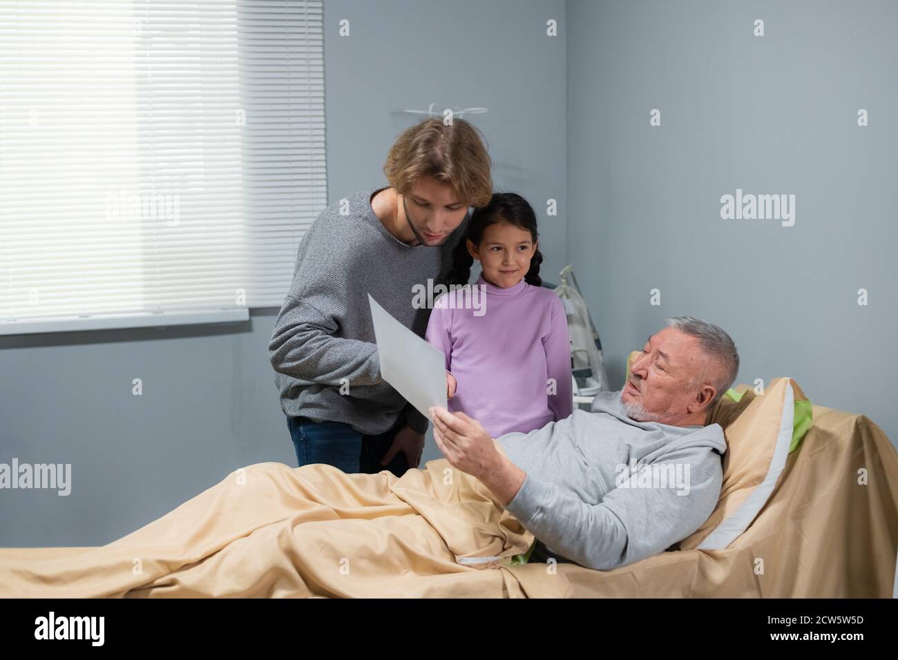 Nipoti, una bambina e il fratello maggiore, che visitano il nonno in un reparto ospedaliero. Foto Stock