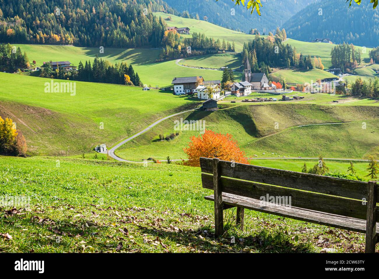 La panchina con vista panoramica sul paese di Santa Magdalena, nel nord Italia, sulle pendici delle Dolomiti nella valle della Val di Funes. Foto Stock
