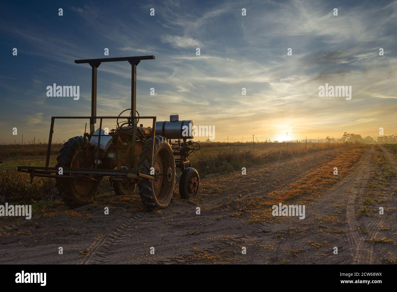 Un vecchio trattore agricolo è inutilizzato, bagnato dalla luce del sole che sorge su una strada sterrata accanto ad un paddock pronto per l'aratura a Mareba, Australia. Foto Stock