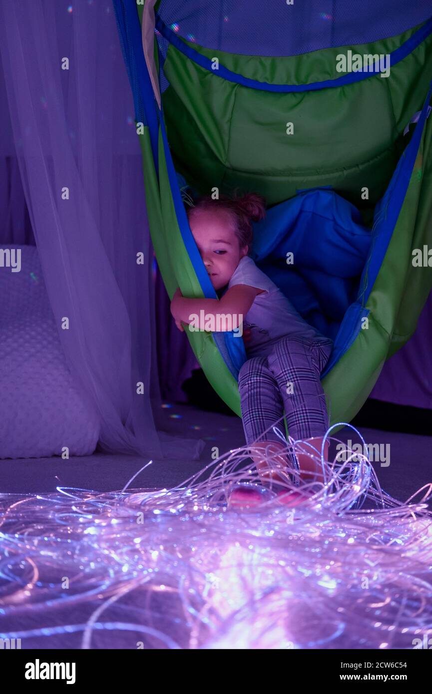 Bambino in terapia sensoriale stimolante sala, snoezelen. Bambino autistico che interagisce con luci colorate durante la sessione di terapia. Foto Stock