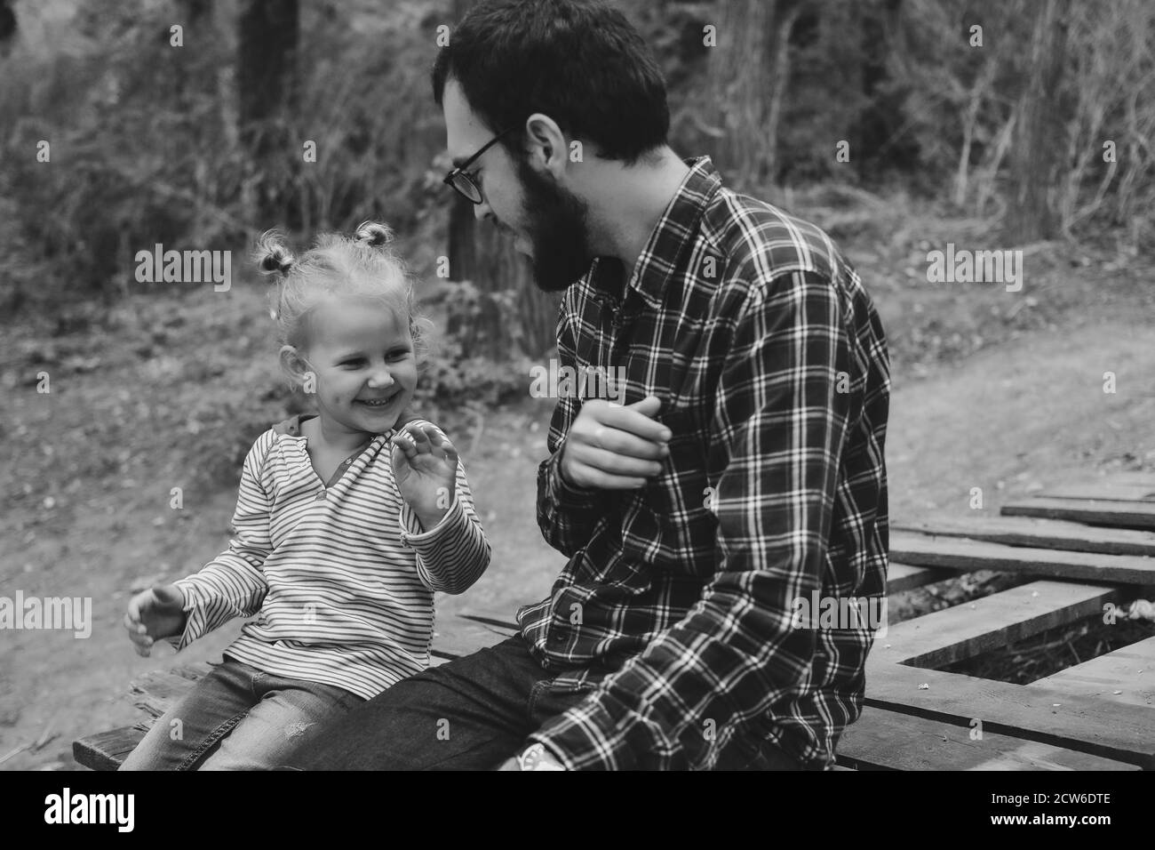 Baby e padre giocano nel parco autunnale. Papà e figlia sono seduti su un ponte di legno all'aperto. Felici momenti di infanzia in famiglia. Foto Stock