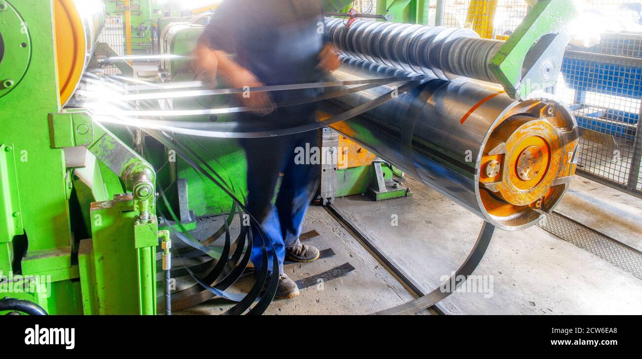 Rotolo di lamiera zincata in macchina da taglio, fabbrica di ferri e metallurgia per la produzione di tubi e tubi in metallo con il lavoratore. Foto Stock