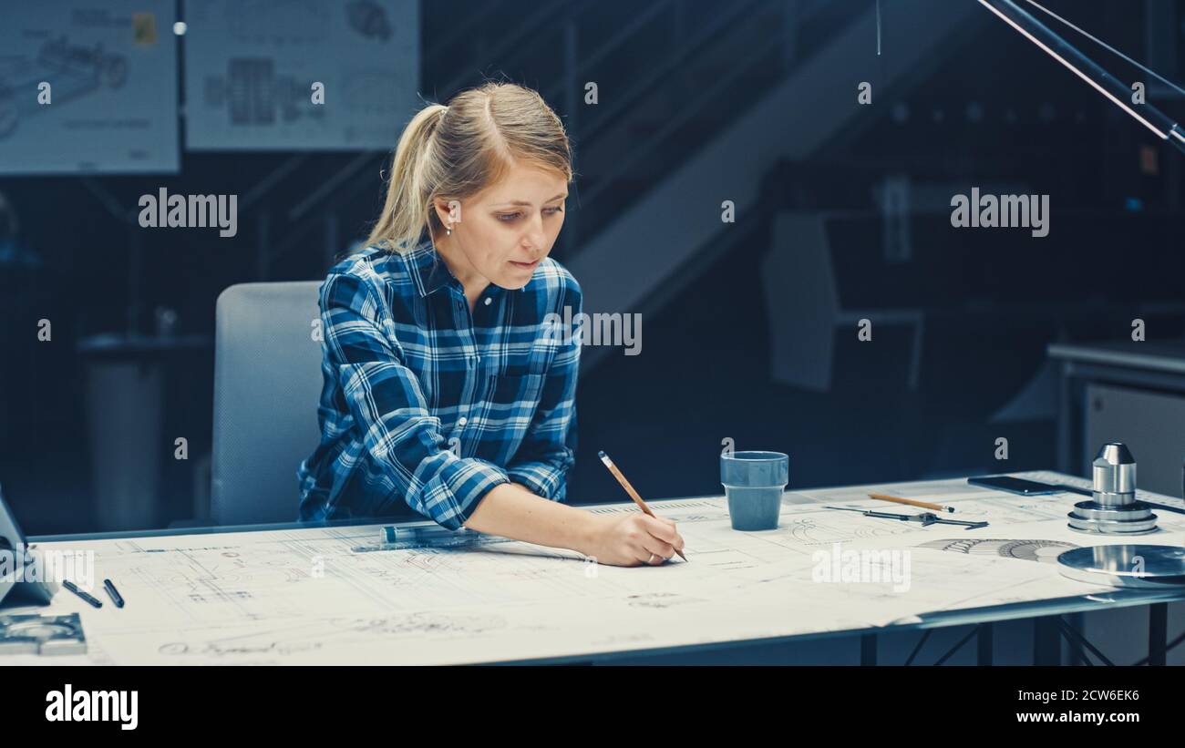 Ingegnere femminile seduto alla sua scrivania lavora con Blueprints che posano su un tavolo, usa Pencil, Ruler e Tablet digitale. Nel Dark Industrial Design Foto Stock