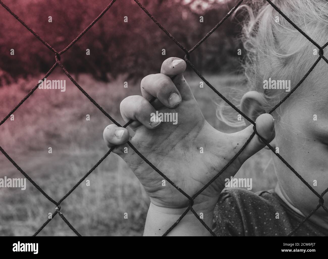Il bambino tiene una recinzione di ferro con la mano. Triste bambino. Crudeltà verso i bambini. Blacck e bianco Foto Stock