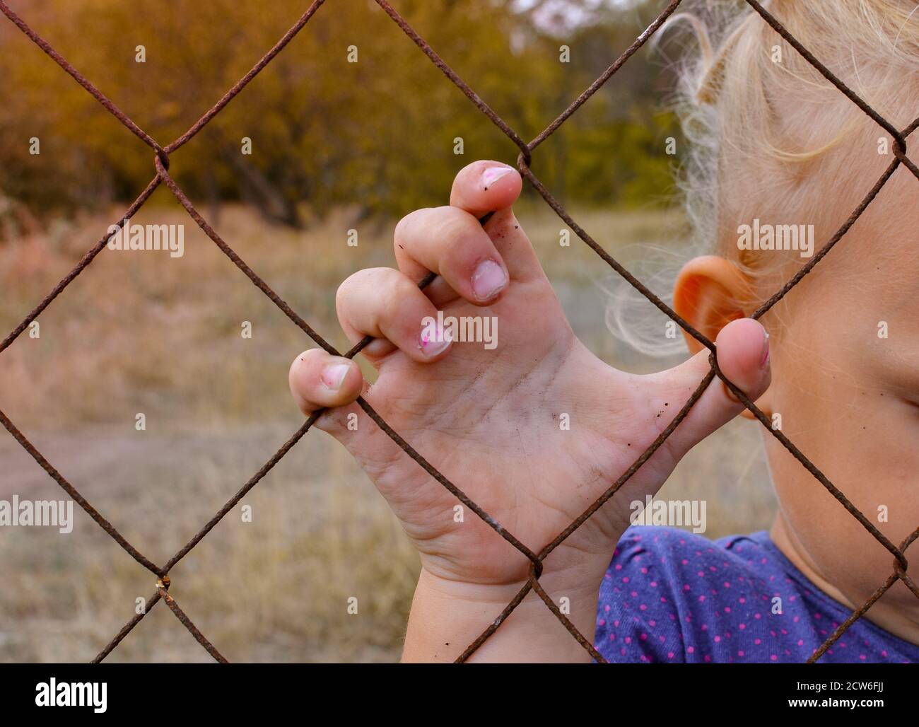 Il bambino tiene una recinzione di ferro con la mano. Triste bambino. Crudeltà verso i bambini. Foto Stock