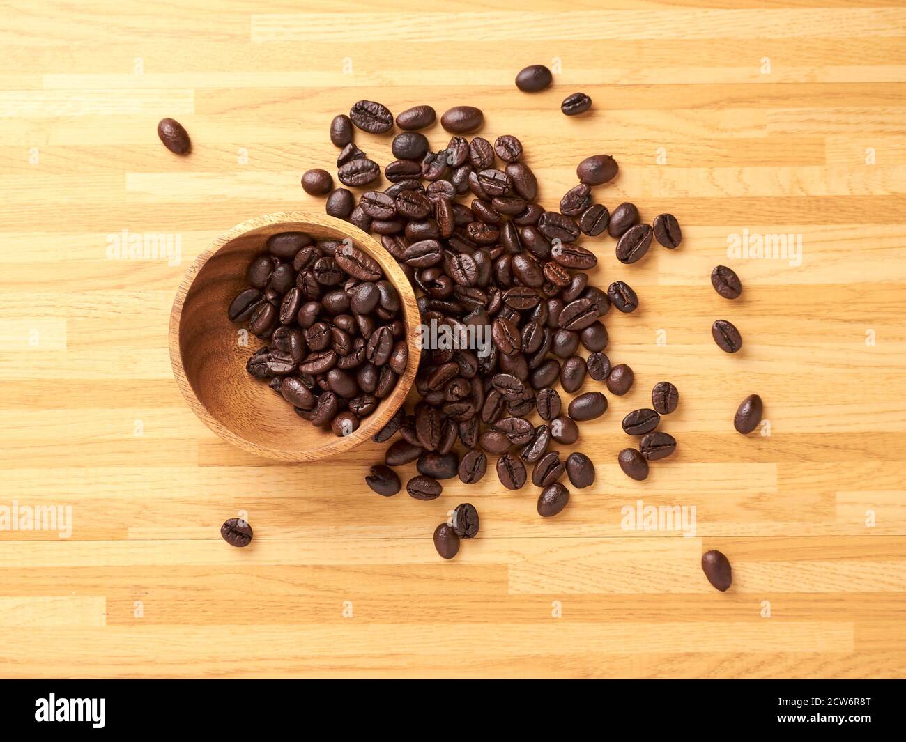 Una raccolta di chicchi di caffè in un recipiente di legno e. più sparsi all'esterno Foto Stock