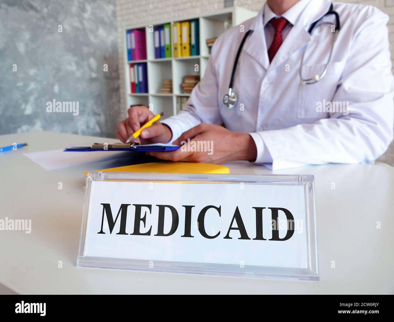 Un piatto con un'iscrizione Medicaid e un medico che compila i documenti. Foto Stock