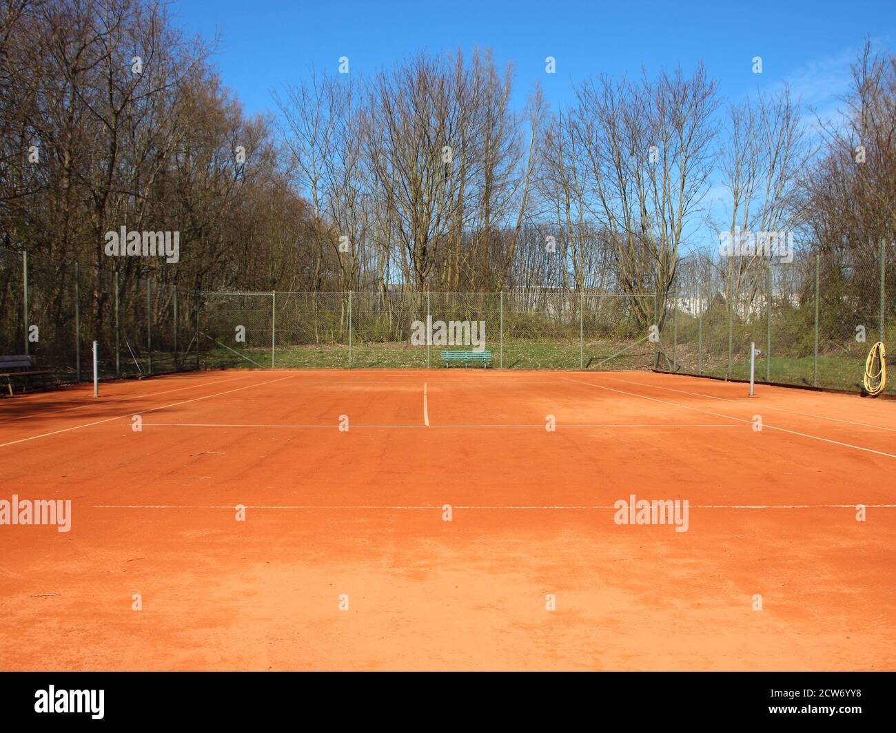 Un campo da tennis vuoto in terra rossa in estate. Non c'è rete, e il cortile è circondato da una recinzione con alberi sullo sfondo. Foto Stock