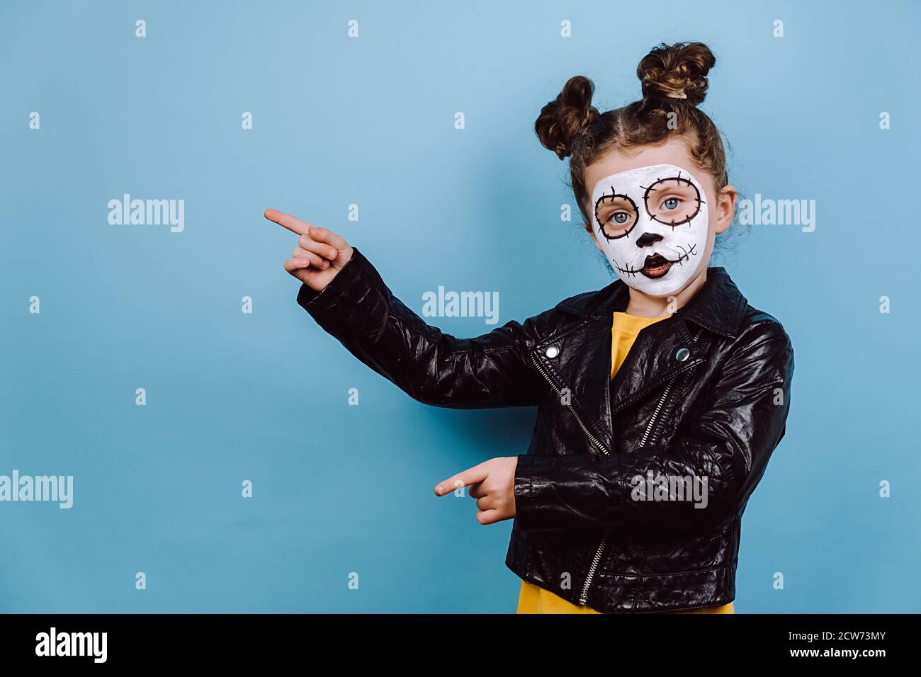 Cultura messicana, concetto giorno della morte. Ritratto di cute piccola ragazza con trucco spaventoso luminoso, punti da parte su blu studio copia spazio, vestito in nero Foto Stock