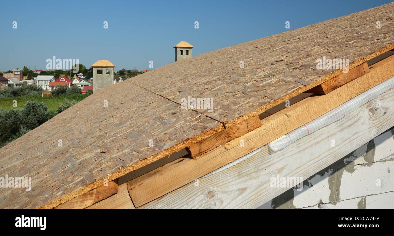 Un primo piano sulla costruzione di tetti, rivestimenti di tetti con pannelli in legno compensato, OSB e vapore, membrana a prova di umidità su travi di tetto contro cielo blu. Foto Stock