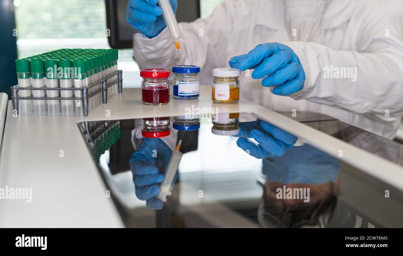 Ricercatore in laboratorio. Fluidi colorati in flaconi e provette verdi. Vetro dell'analizzatore lucido con riflesso dell'assistente di laboratorio con una siringa in mano. Foto Stock