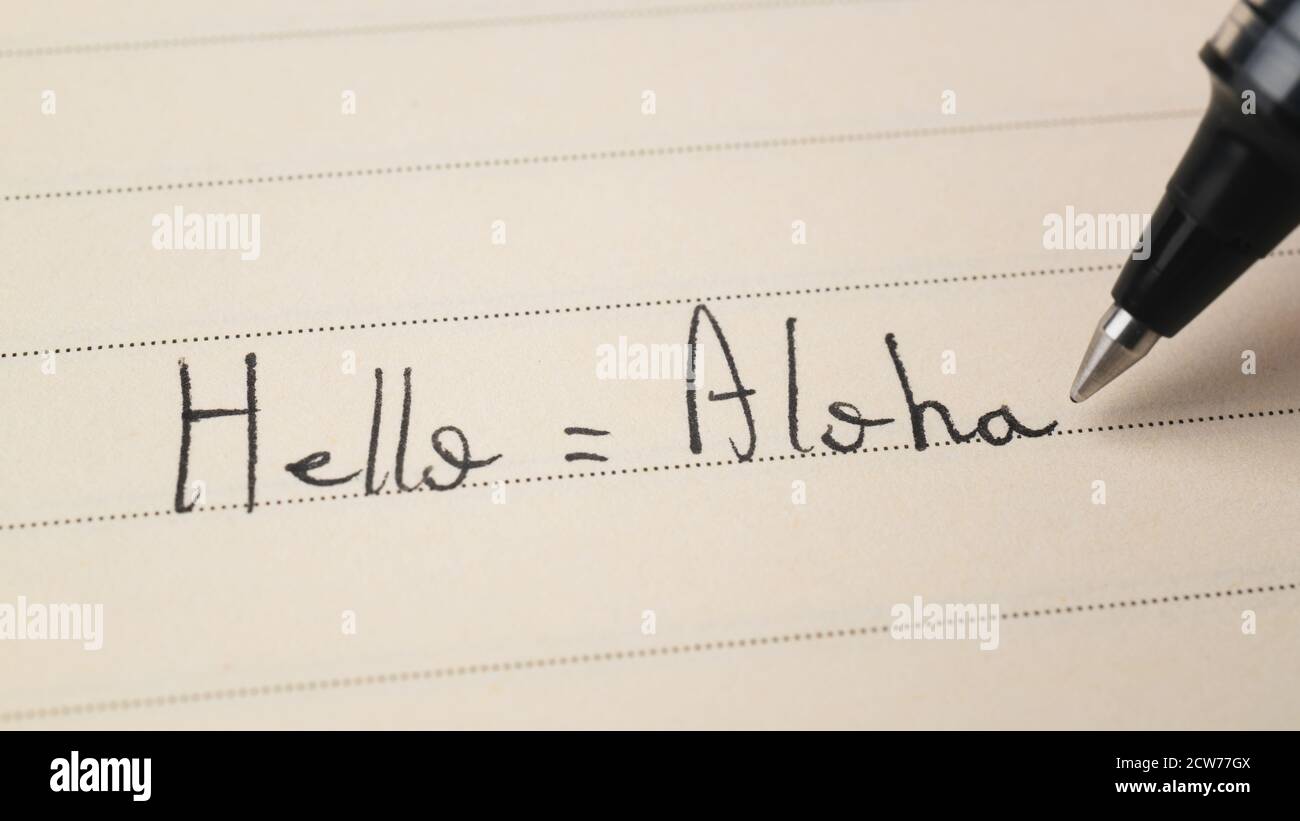 Principiante studente di lingua hawaiana che scrive Ciao parola Aloha per i compiti su uno scatto macro del notebook Foto Stock