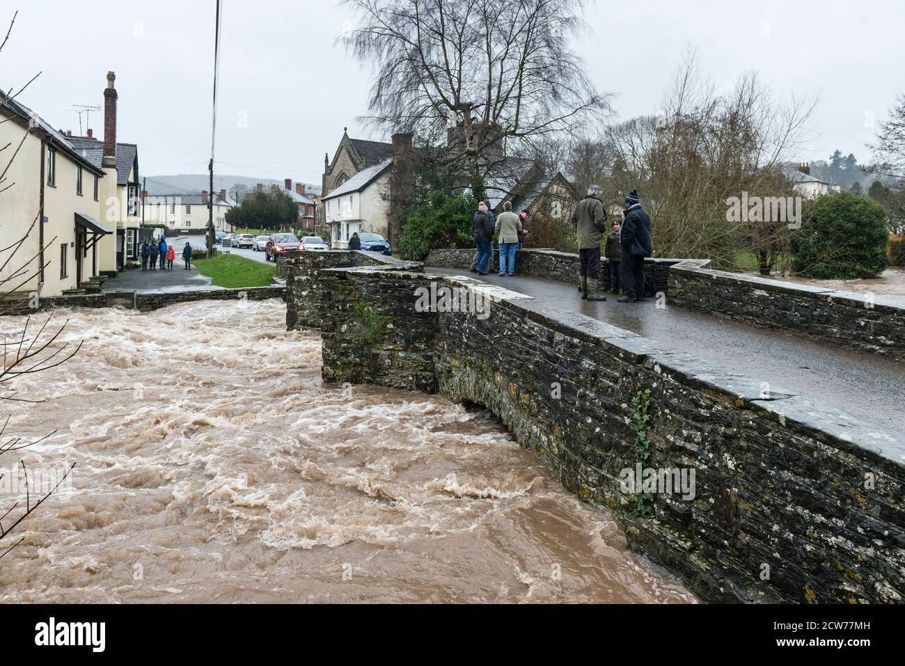 Gli spettatori si riuniscono sul vecchio ponte 17c sul fiume Lugg a Presteigne, Powys, Regno Unito, per vedere il più alto livello di alluvione dopo Storm Dennis all'inizio del 2020 Foto Stock