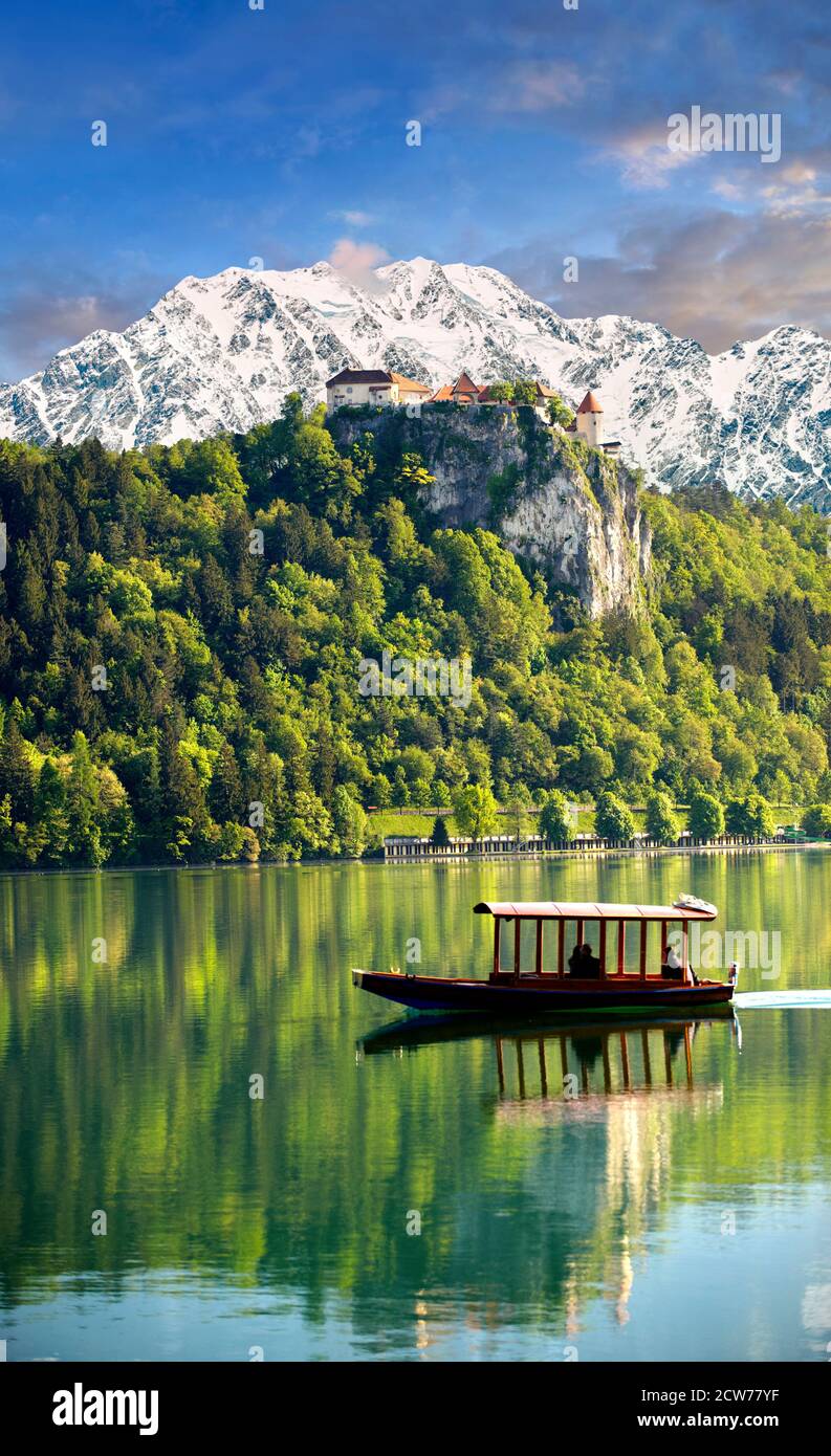 Lago di Bled con il castello di Bled con le cime innevate dell'apline alle spalle e una barca dal fondo piatto chiamata Pletna. Bled Slovania. Foto Stock