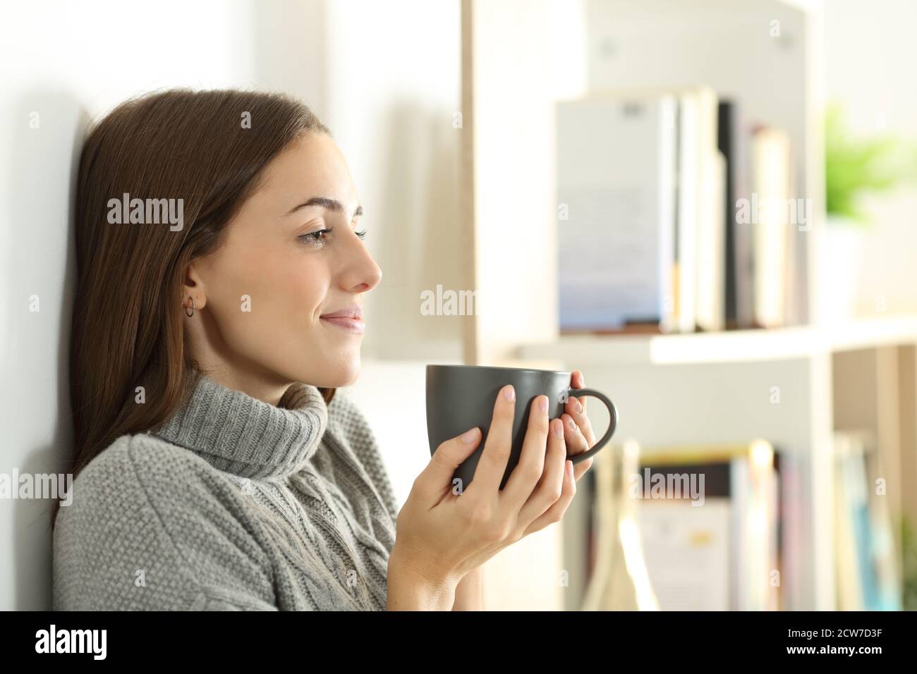 Profilo di una donna rilassata guarda via nella tenuta invernale tazza di caffè in piedi a casa Foto Stock