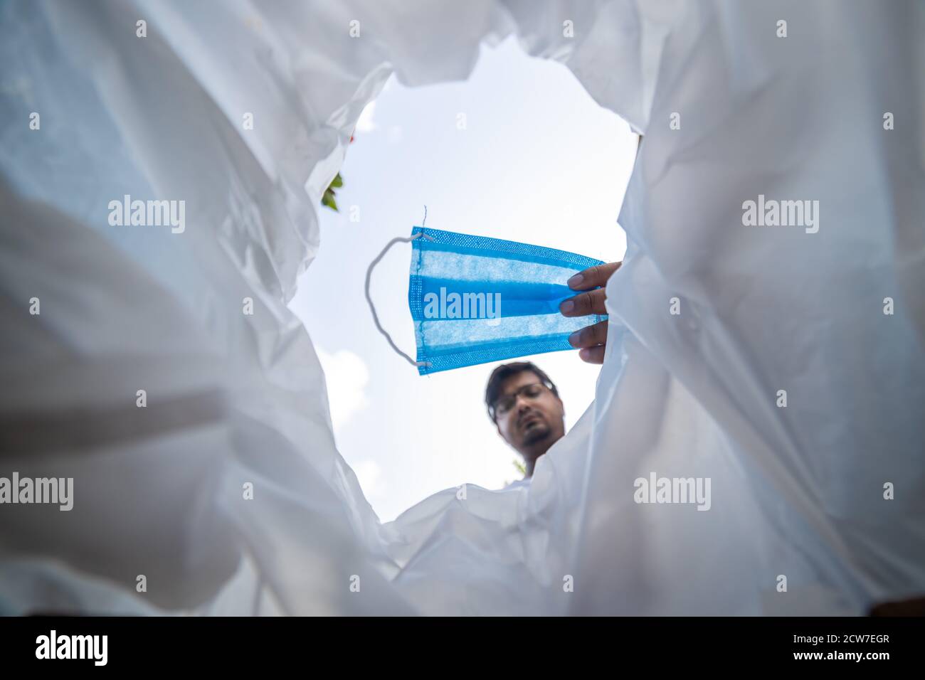 Vista ad angolo basso dell'uomo che getta la maschera facciale usata cestino Foto Stock
