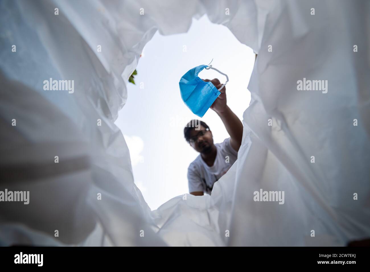 Vista ad angolo basso dell'uomo che getta la maschera facciale usata cestino Foto Stock