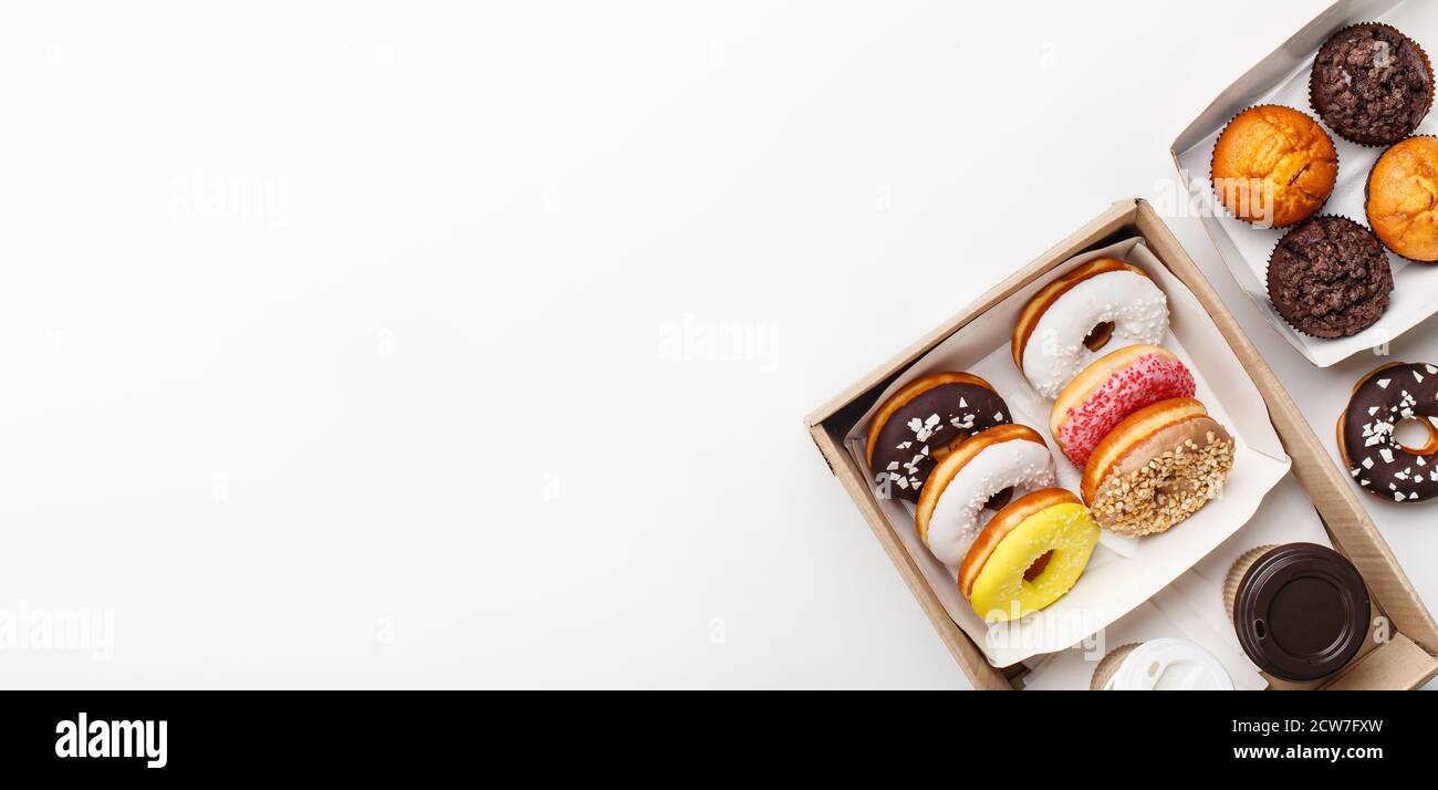 Dolci, malsani e fast food. Ciambelle con diversi smalto, cupcakes e muffin al cioccolato in scatole e due caffè in tazze di carta da andare Foto Stock